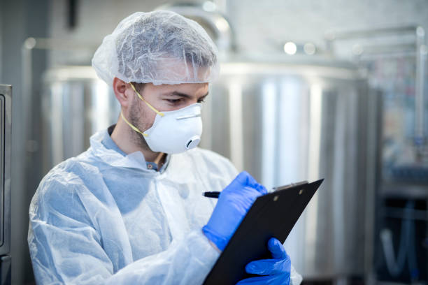 istock Technologist in white suit wearing hairnet and protective mask checking production in industrial factory. 1097346500