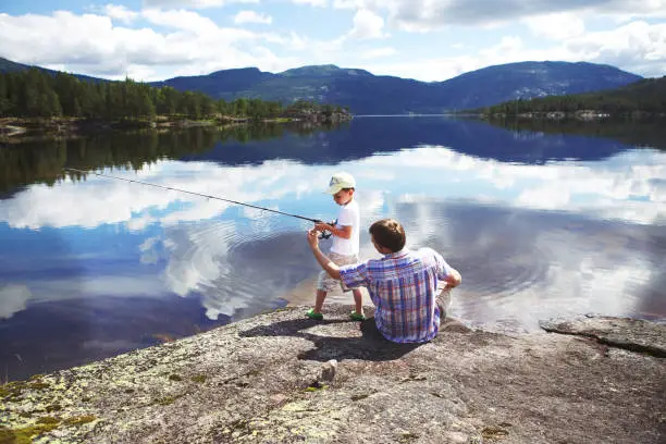 Photo of Father shows his little son how to fish. Norway, summer.