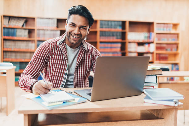 istock Smiling student with laptop and textbook in a library 1097354082