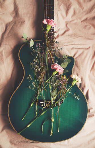 High angle shot of a green guitar lying on a bed with flowers arranged on it