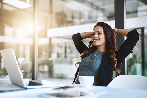 Cropped shot of an attractive young businesswoman sitting with her hands behind her head at her desk in the office