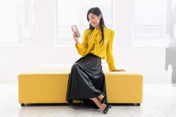 donna cinese su panchina gialla con telefono - black skirt foto e immagini stock