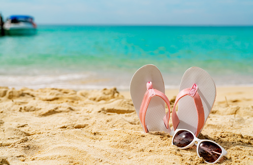 Pink and white sandals, sunglasses on sand beach at seaside. Casual fashion style flipflop and glasses at seashore. Summer vacation on tropical beach. Fun holiday travel on sandy beach. Summertime.