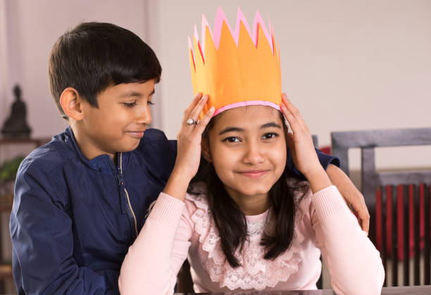 Sad boy with happy sister wearing crown at home
