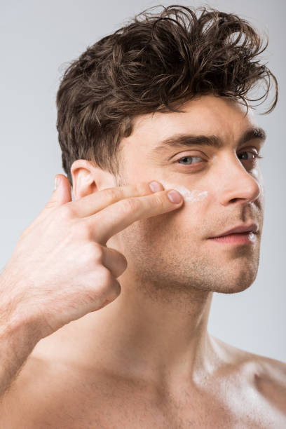 istock handsome man applying cosmetic cream on face, isolated on grey 1097381344