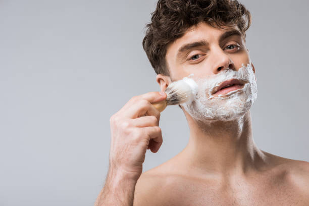 istock handsome young man applying shaving foam with brush, isolated on grey 1097383886