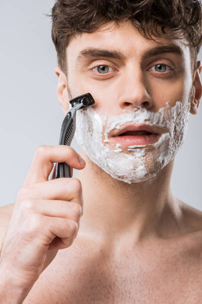 istock young man foam on face shaving with razor, isolated on grey 1097383896