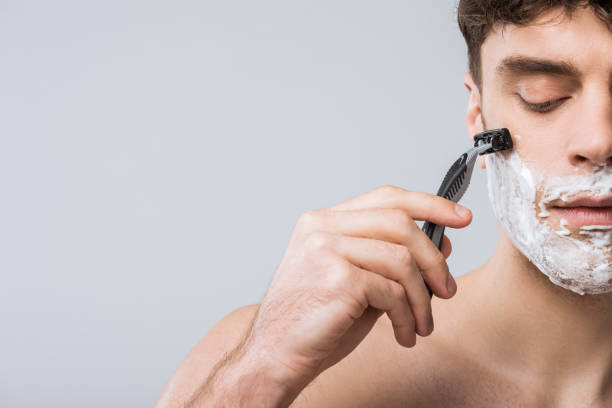 handsome young man foam on face shaving with razor, isolated on grey