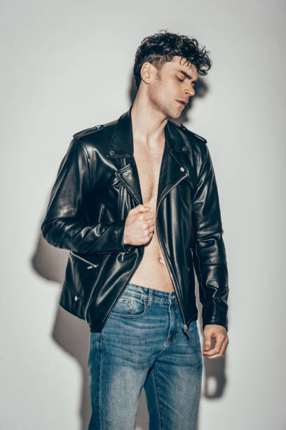 istock handsome stylish man posing in jeans and black leather jacket on grey 1097383986