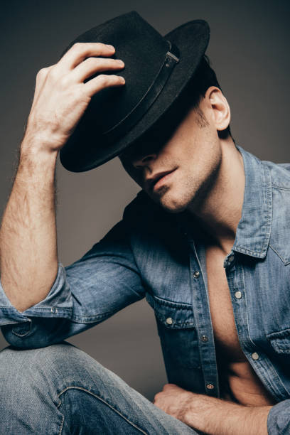 istock handsome man in denim shirt posing with hat isolated on dark grey 1097385170