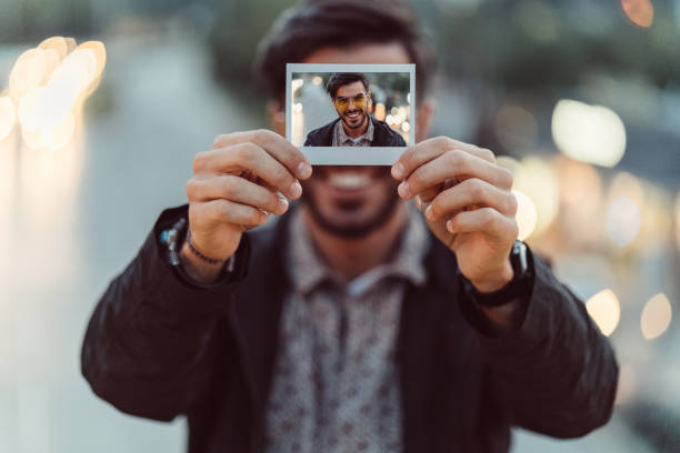 Young man showing instant self-portrait Man showing polaroid portrait to the camera showing photos stock pictures, royalty-free photos & images