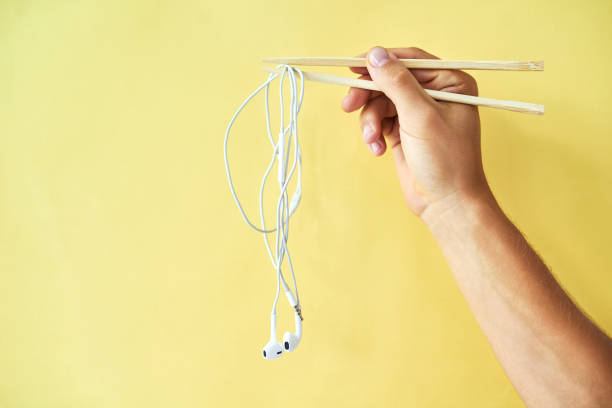 Cropped studio shot of a man holding earphones wrapped around chopsticks against a yellow background
