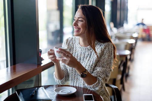 Young beautiful happy woman drinking coffee in restaurant