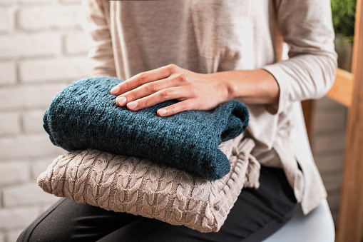 Woman's hands holding knitted clothes. Close up. Concept of cozy home.
