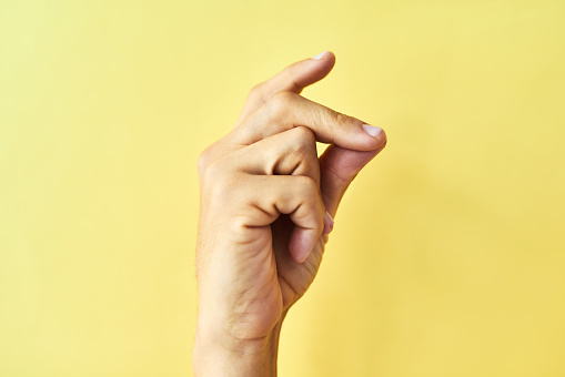 Studio shot of an unrecognizable man snapping his fingers against a yellow background