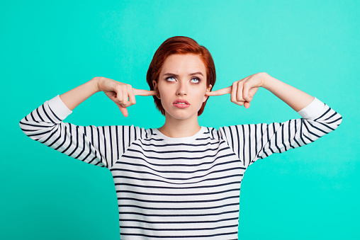 Portrait of nice pretty charming attractive sad red-haired lady wearing striped pullover rolling eyes up closing ears with forefingers isolated over bright vivid shine green turquoise background