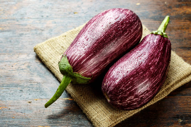 istock two ripe motley eggplants on a wooden table, lying on burlap. 1097428560