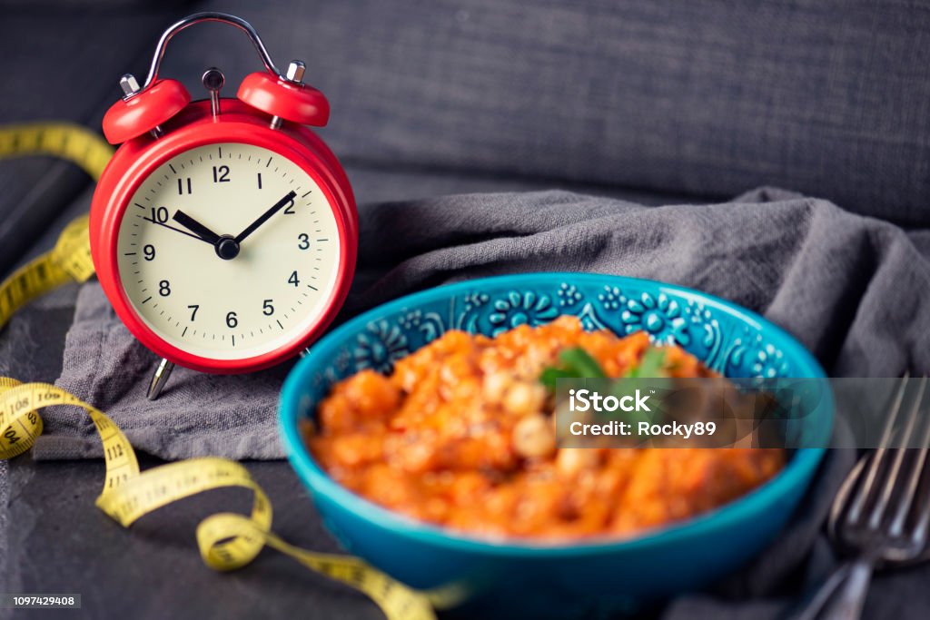 Intermittent Fasting – Weight Loss Losing weight with intermittent fasting gets more and more popular, here showed with a clock and traditional, vegan Chana Alu Masala, an indian dish Intermittent Fasting Stock Photo