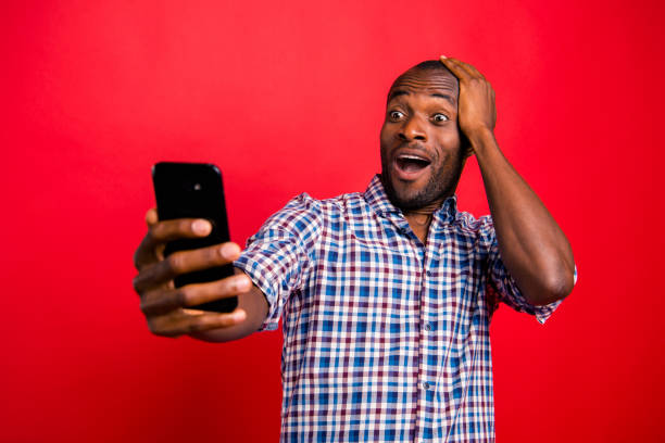 Portrait of nice funny crazy handsome attractive cheerful guy wearing checkered shirt holding in hands cell reading gadget device isolated over bright vivid shine red background Portrait of nice funny crazy handsome attractive cheerful guy wearing checkered shirt holding in hands cell reading gadget device isolated over bright vivid shine red background stubble male african ethnicity facial hair stock pictures, royalty-free photos & images