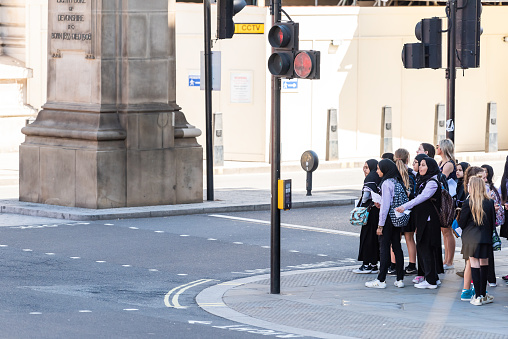 London, UK - June 22, 2018: Many people tourists school children muslim girls standing waiting at crosswalk to cross street during day by road in city