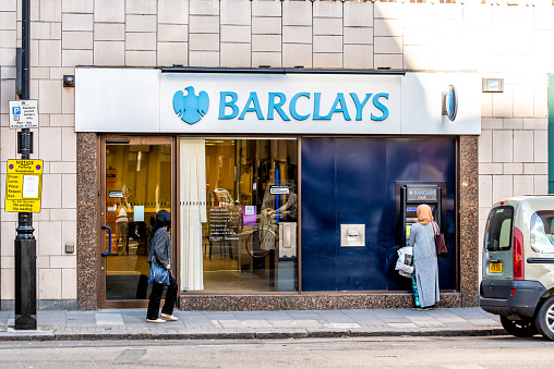 London, UK - June 21, 2018: Blue Barclays bank cash sign atm with people woman walking at banking branch office building entrance in Westminster on sidewalk