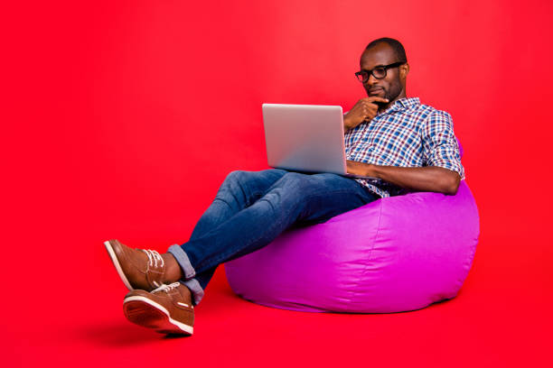 istock Nice calm focused concentrated handsome guy wearing checked shirt working remotely on laptop creating presentation sitting on violet bag isolated over bright vivid shine red background 1097437768