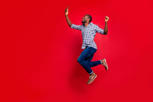 comprimento total corpo tamanho perfil vista de lado legal engraçado bonito alegre maluco vestindo camisa quadriculada segurando na cela de mãos, lendo o texto no ar isolado no fundo vívido brilho vermelho - jumping people - fotografias e filmes do acervo