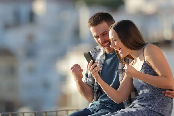 Photo of Excited couple celebrating online phone news outdoors