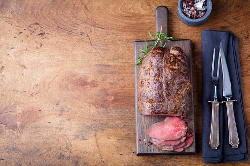 Roast beef on cutting board. Wooden background. Top view. Copy space