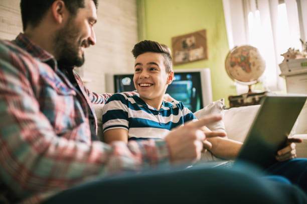 istock Smiling father and son using digital gadgets in living room 1097465428