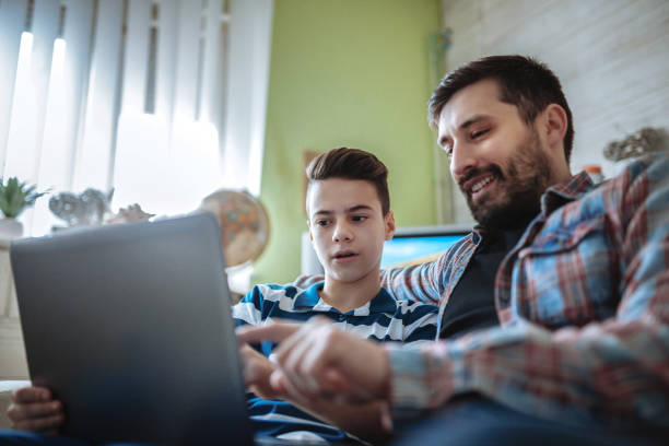 istock Smiling father and son using digital gadgets in living room 1097465512