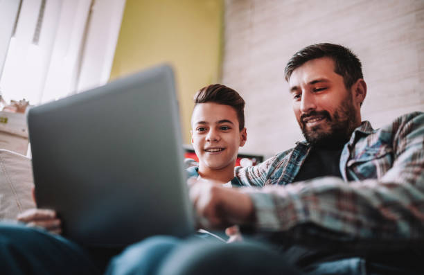 istock Smiling father and son using digital gadgets in living room 1097465882