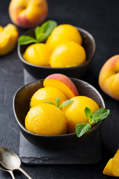 Mango, peach ice cream, tropical fruit sorbet in black bowl on stone background.