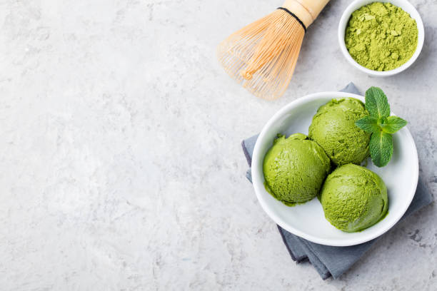 Green tea matcha ice cream scoop in white bowl on a grey stone background. Copy space. Top view