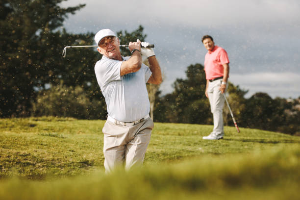 Pro golfer playing on the course Pro golfer playing on the course with second player standing at back looking on. Man hitting the ball out of a sand bunker during the game. golfer stock pictures, royalty-free photos & images