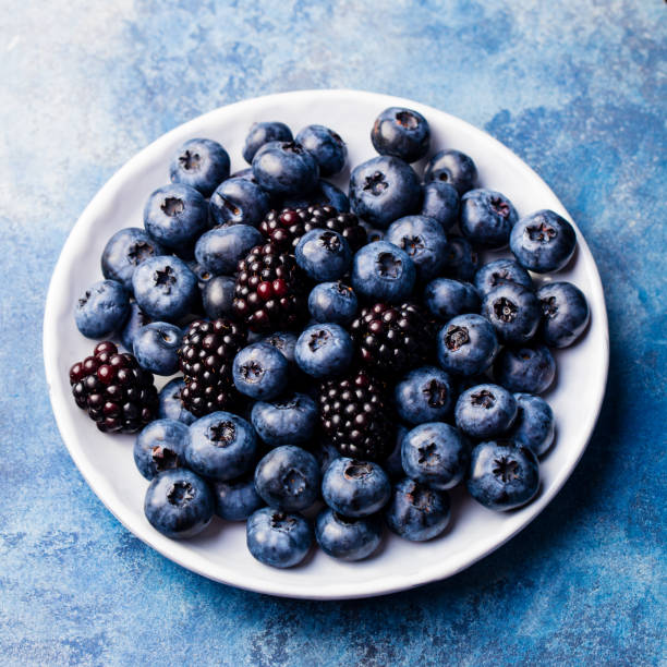 istock Blueberry and blackberry berries on a white plate on blue stone background. Top view. 1097473202