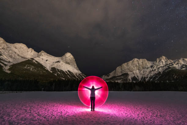 ピンクの光の山の下の雪原に立っている女性 - rocky mountains flash ストックフォトと画像