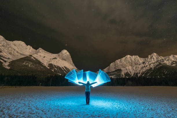 青い光の山の下の雪原に立っている女性 - rocky mountains flash ストックフォトと画像