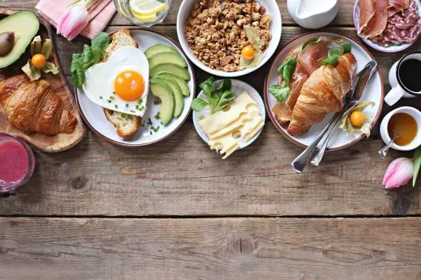 Breakfast food table. Festive brunch set, meal variety with fried egg, croissant sandwich, granola and smoothie. Overhead view