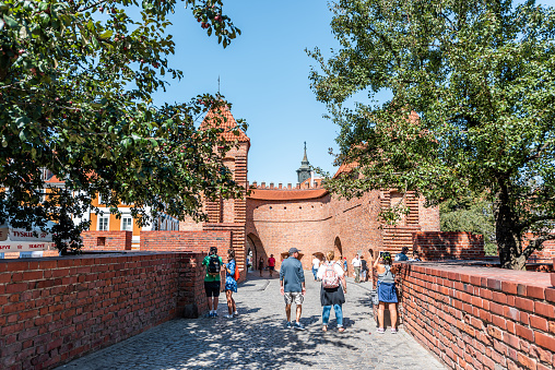 Warsaw, Poland - August 22, 2018: Famous old town historic street in capital city during sunny summer day and red orange brick wall fortress people walking on bridge