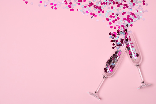 two glasses with confetti hearts on pink background