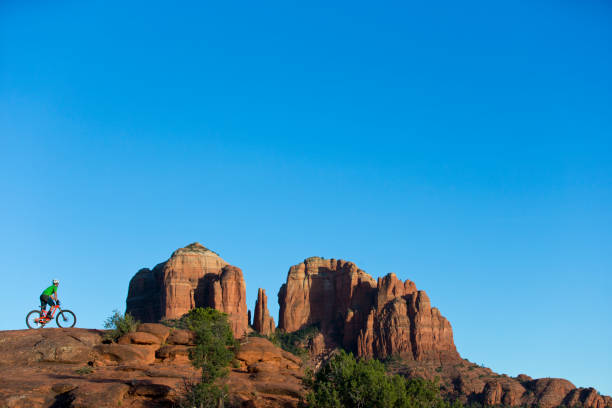 A man rides a popular trail in Sedona, Arizona, USA. He is riding an enduro-style mountain bike. The Cathedral Rock landmark is in the background.