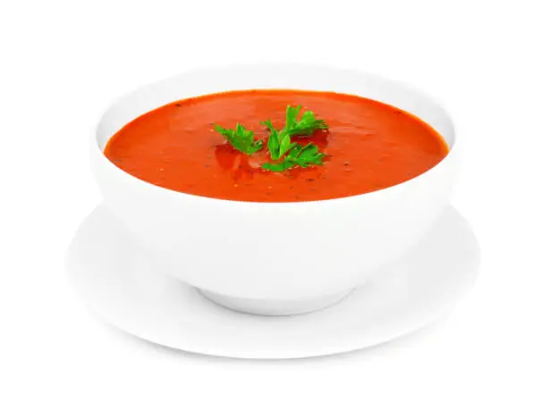 Homemade tomato soup in a white bowl with saucer. Side view isolated on a white background.