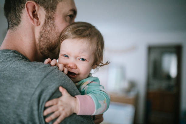 Father Holding Infant Sick With Cold Virus Cold and flu season takes its toll, with babies and small children even more susceptible to illness.  A dad holds his baby girl, trying to comfort her in the midst of her sickness. genderblend stock pictures, royalty-free photos & images