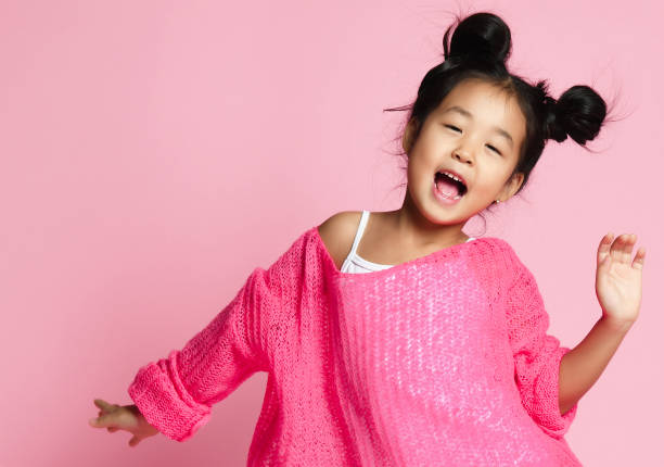 Asian kid girl in pink sweater, white pants and funny buns sings. close up. stock photo