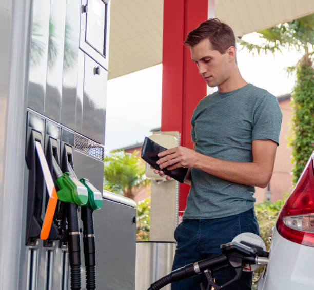 giovane bell'uomo controllando il suo portafoglio durante il rifornimento di benzina - utility payments foto e immagini stock