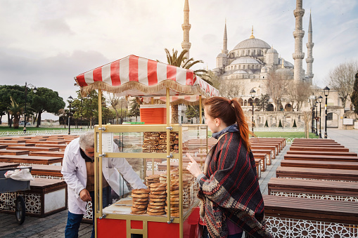 Istanbul, Turkey - March 31, 2017: Happy beautiful tourist woman buy traditional turkish simit or bagel food and walking on Istanbul street, Turkey