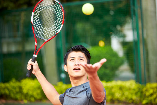 молодой азиатский человек, играющий в теннис - tennis serving men court стоковые фото и изображения