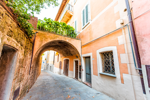 Chiusi, Italy street in small historic medieval town village in Umbria during sunny day with nobody orange yellow pink vibrant colorful walls and arch