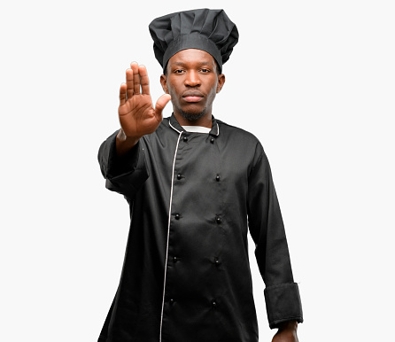 Young black cook wearing chef hat annoyed with bad attitude making stop sign with hand, saying no, expressing security, defense or restriction, maybe pushing